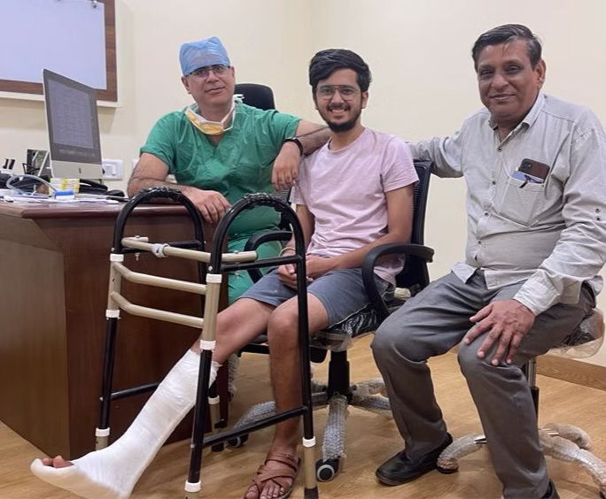 Surgeon and smiling patient with leg cast and walker, alongside a family member in clinic office